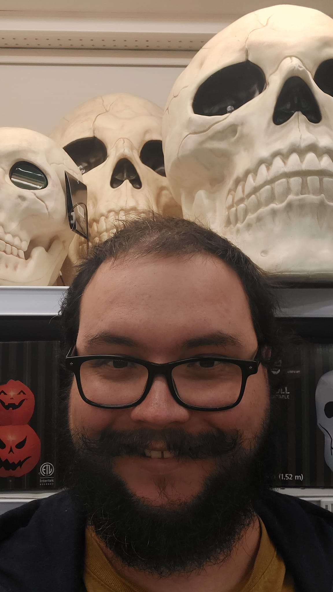 A man with short hair and bushy facial hair stands in front of some large plastic skulls